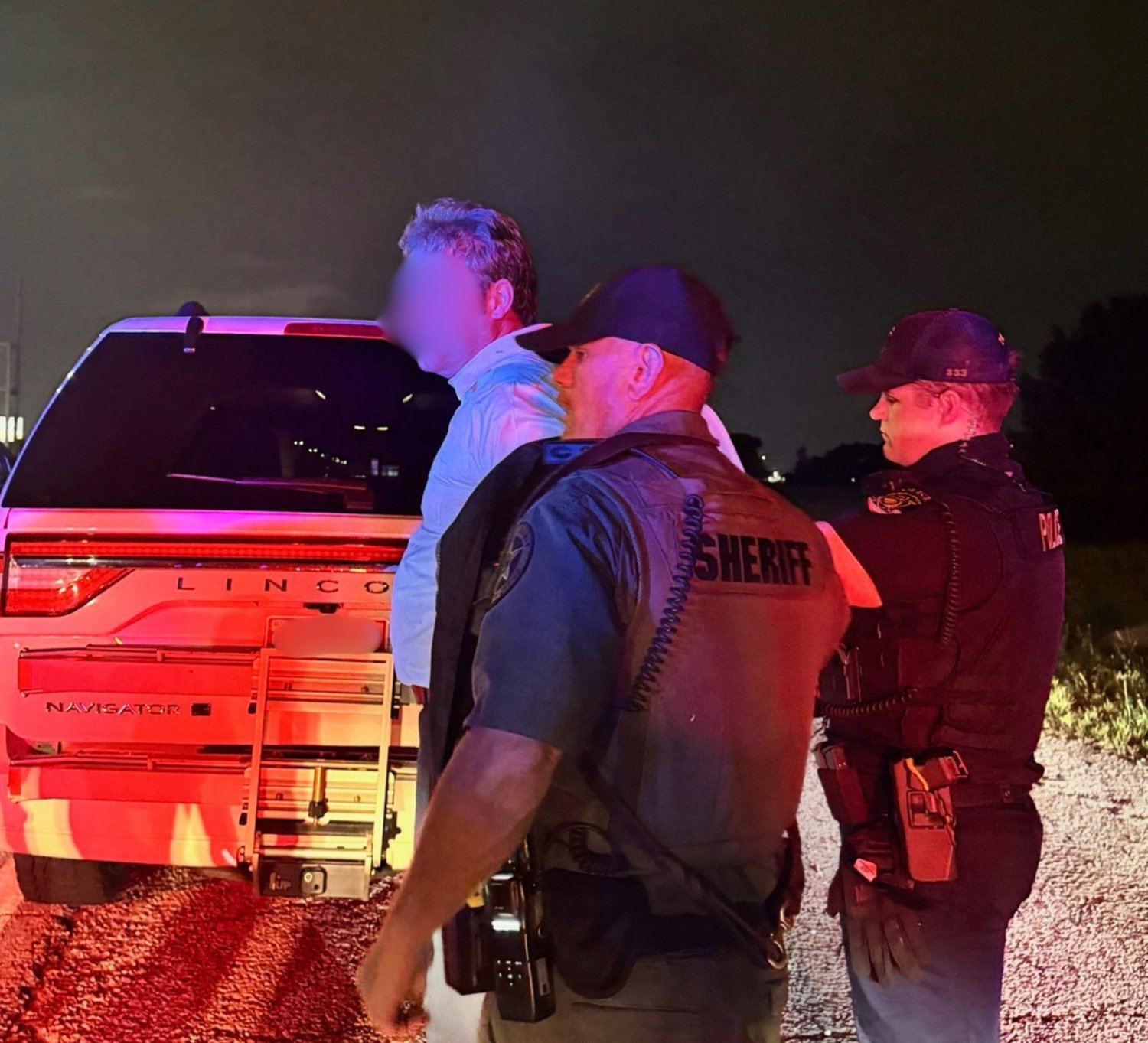 Officers detaining a suspect beside a vehicle during a night arrest
